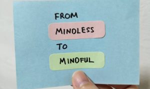 Hand holding a note showing the words From Mindless To Mindful